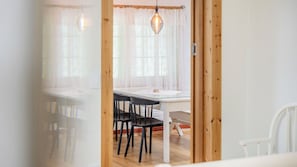 A dining area with a table and chairs, a hanging light fixture, and a view through a doorway.