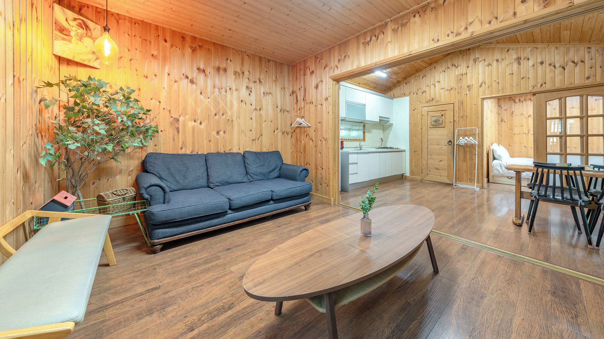 Une pièce chaleureuse avec un plancher en bois, un canapé, une table à manger et un coin cuisine visible à travers une porte ouverte.