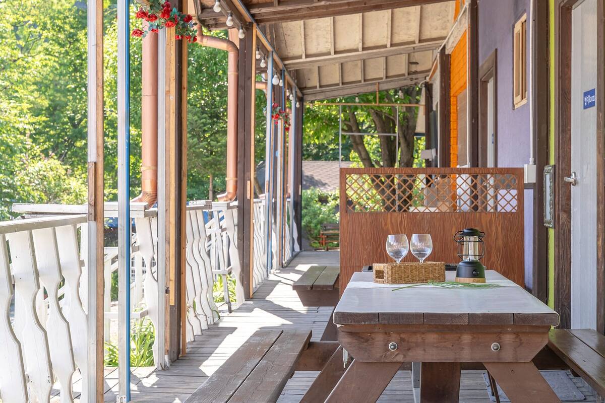 A wooden deck with a table set for two, featuring a basket, two wine glasses, and a portable stove.
