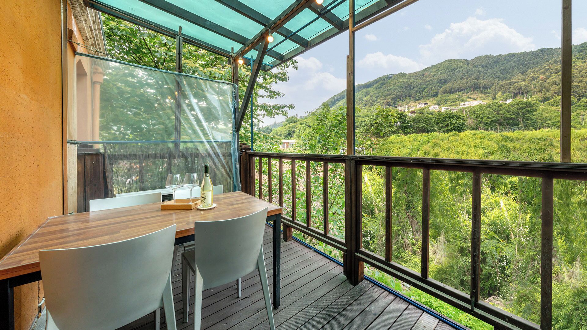 A balcony with a wooden table and chairs, overlooking a lush green landscape with hills in the distance.
