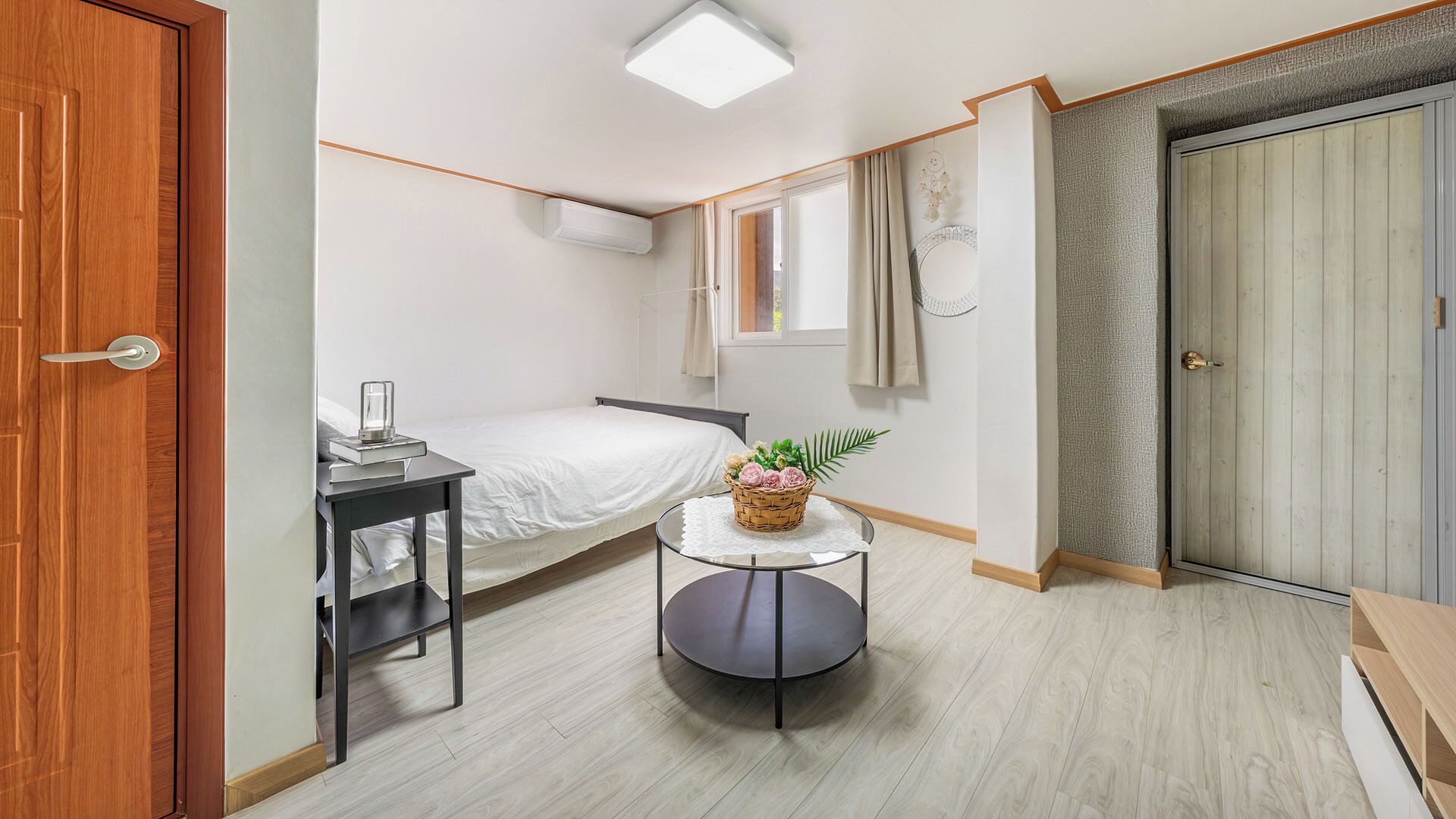 A compact bedroom with a bed, bedside table, and a small round table with a basket of flowers.