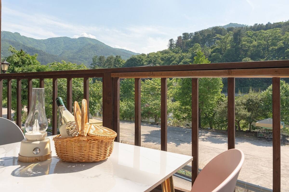 A balcony with a table, chairs, a wicker basket, and a bottle.