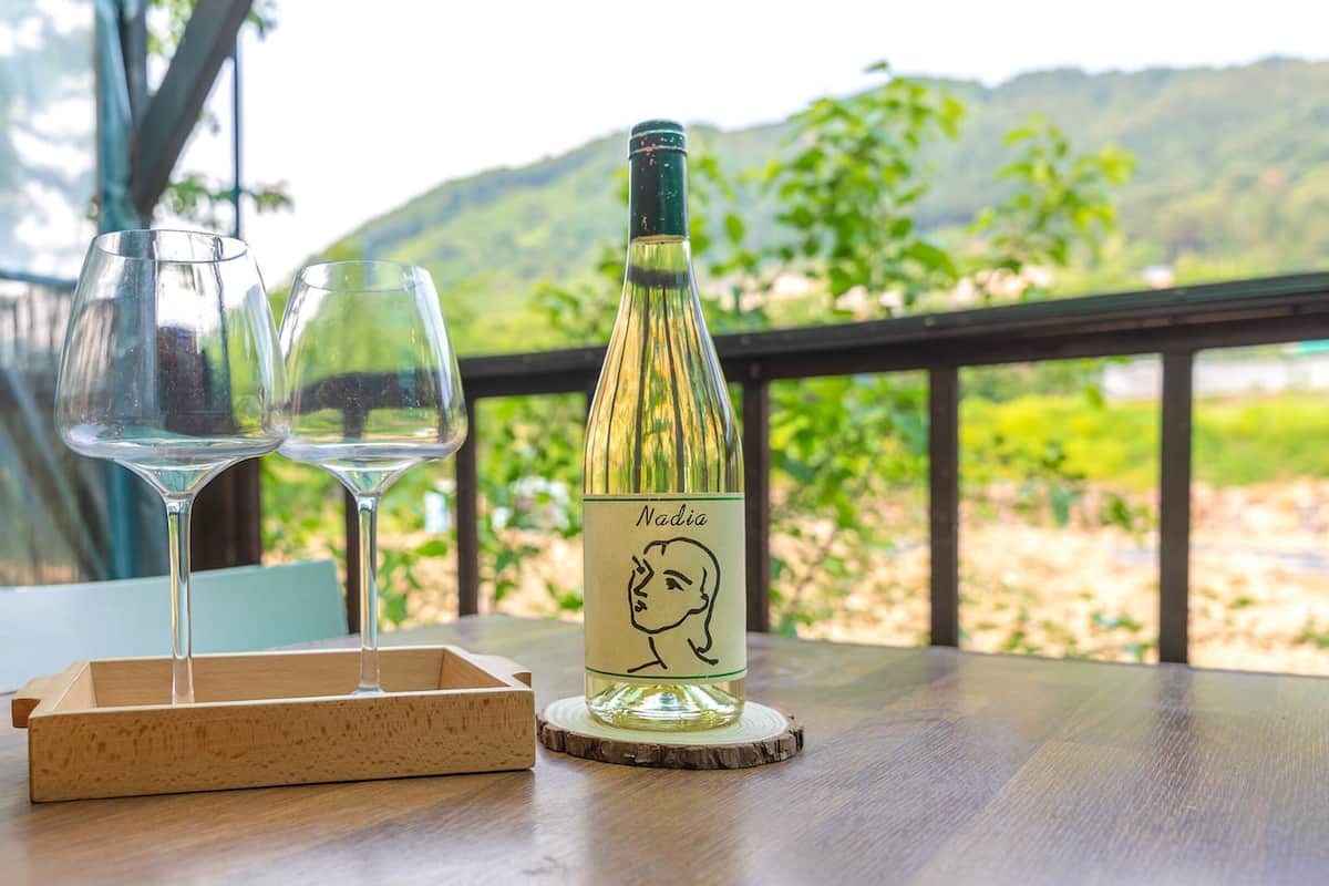 A table with a bottle of wine, two glasses, and a wooden tray.