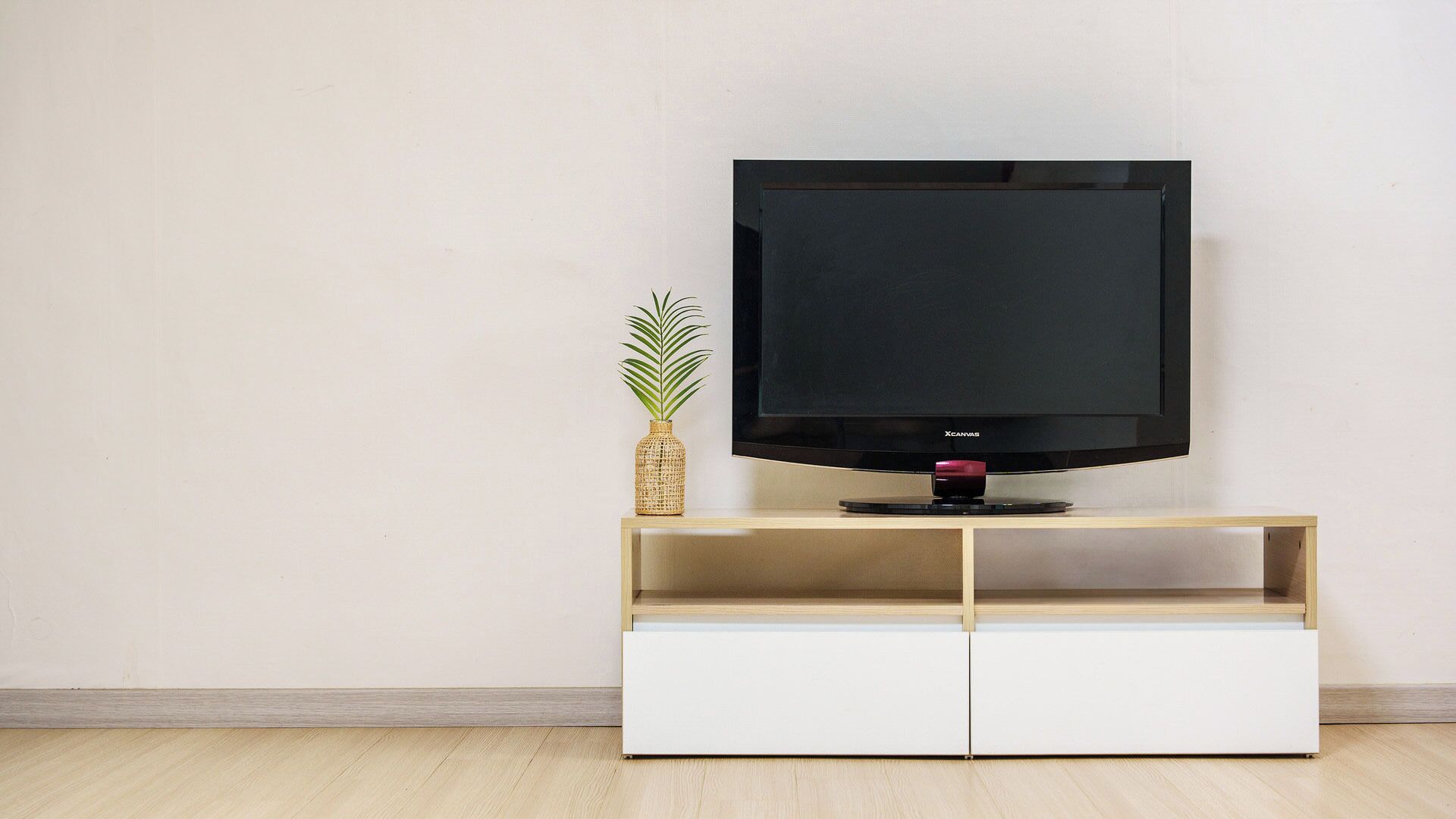 A television on a wooden stand with a plant beside it.