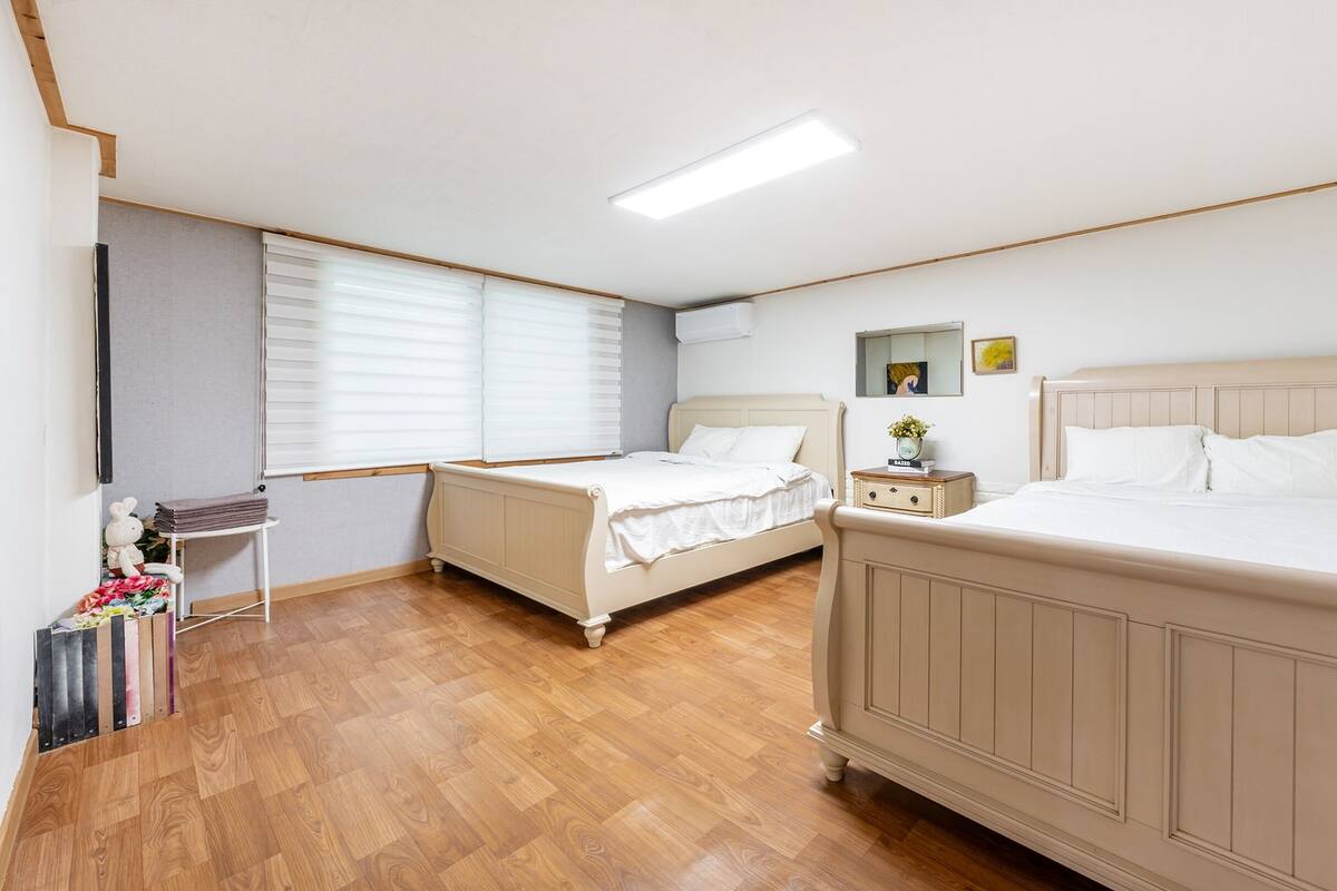 A hotel room with two beds, a small bedside table with a lamp, and a window with blinds.