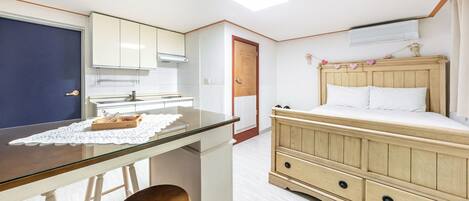 A compact room with a kitchenette, a bed with a wooden headboard, and a small table with a chair.