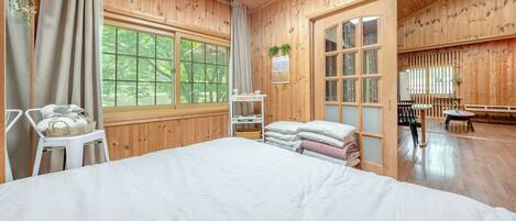 A wooden room with a bed, a chair, a table, and a window with a view of trees.