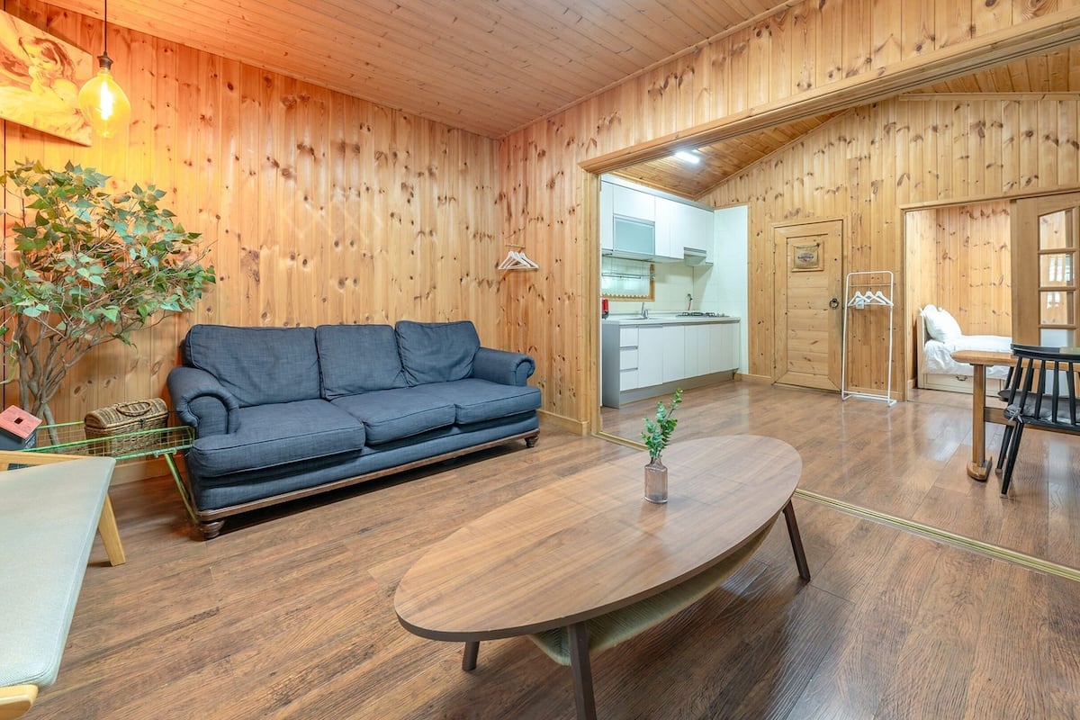A cozy room with a wooden floor, a sofa, a dining table, and a kitchen area visible through an open door.