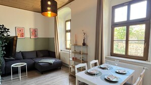 Una sala de estar moderna con techo de madera, un sofá negro, una mesita redonda y una mesa de comedor preparada para cuatro.