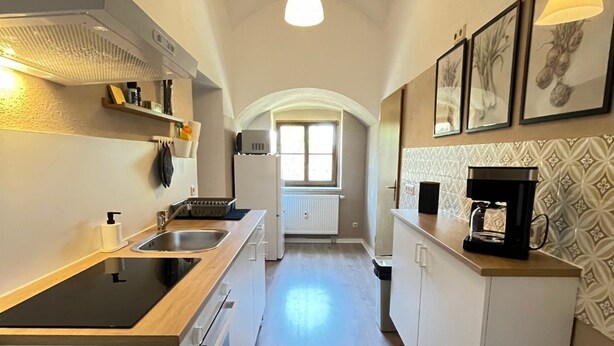 Una cocina estrecha con una isla central, muebles blancos y un ventanal al final.