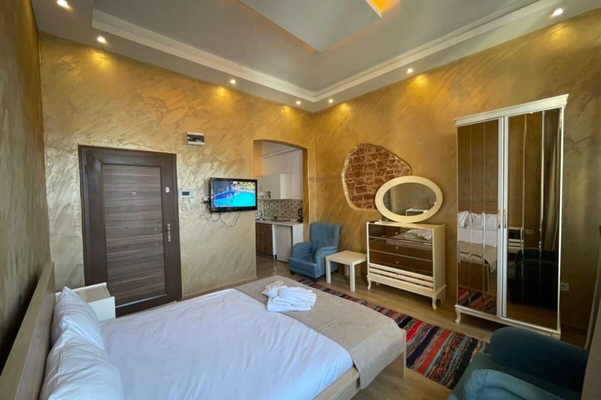 A modern hotel room with a large bed, a TV, a wardrobe, and a seating area.