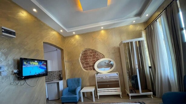 A hotel room with a bed, a TV, a blue armchair, a small table, a mirror, and a wardrobe. - Taksim Stone Wall Apartments (Istanbul)