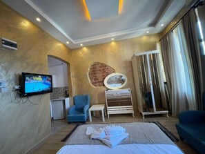 A hotel room with a bed, a TV, a blue armchair, a small table, a mirror, and a wardrobe. - Taksim Stone Wall Apartments (Istanbul)