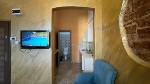 A living room with a television, a blue armchair, and a kitchen area visible through an archway. - Taksim Stone Wall Apartments (Istanbul)
