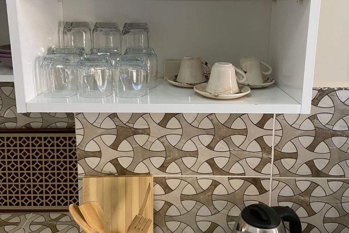 A kitchen with a white shelf holding glassware and a patterned backsplash.