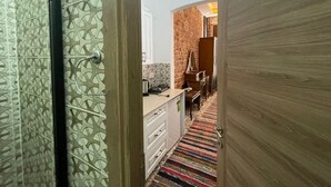 A hallway with a patterned wall, a wooden door, and a kitchen area with a brick wall and wooden cabinets. - Taksim Stone Wall Apartments (Istanbul)