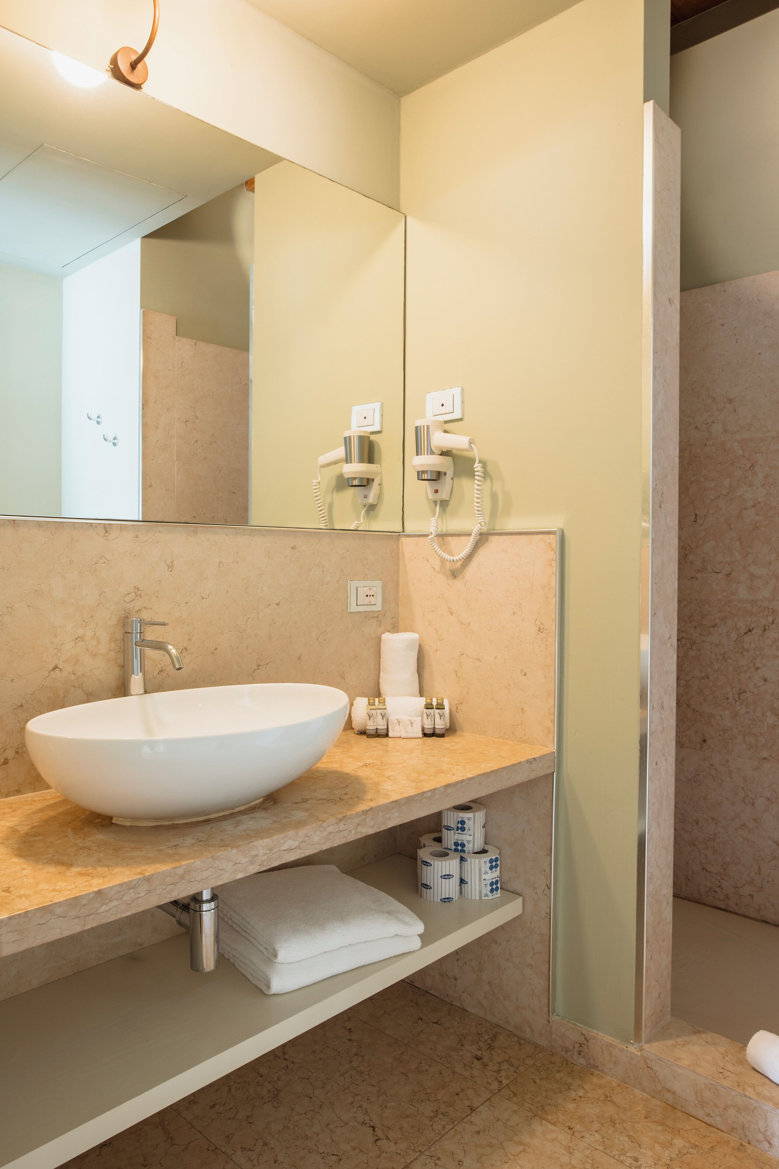 A modern bathroom with a large white sink, a mirror, a towel rack, and a shower area.