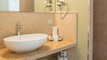 A modern bathroom with a large white sink, a mirror, a towel rack, and a shower area.