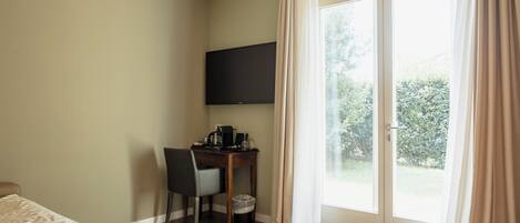 A room with a bed, a desk with a chair, a television, and a sliding glass door to the outdoors.