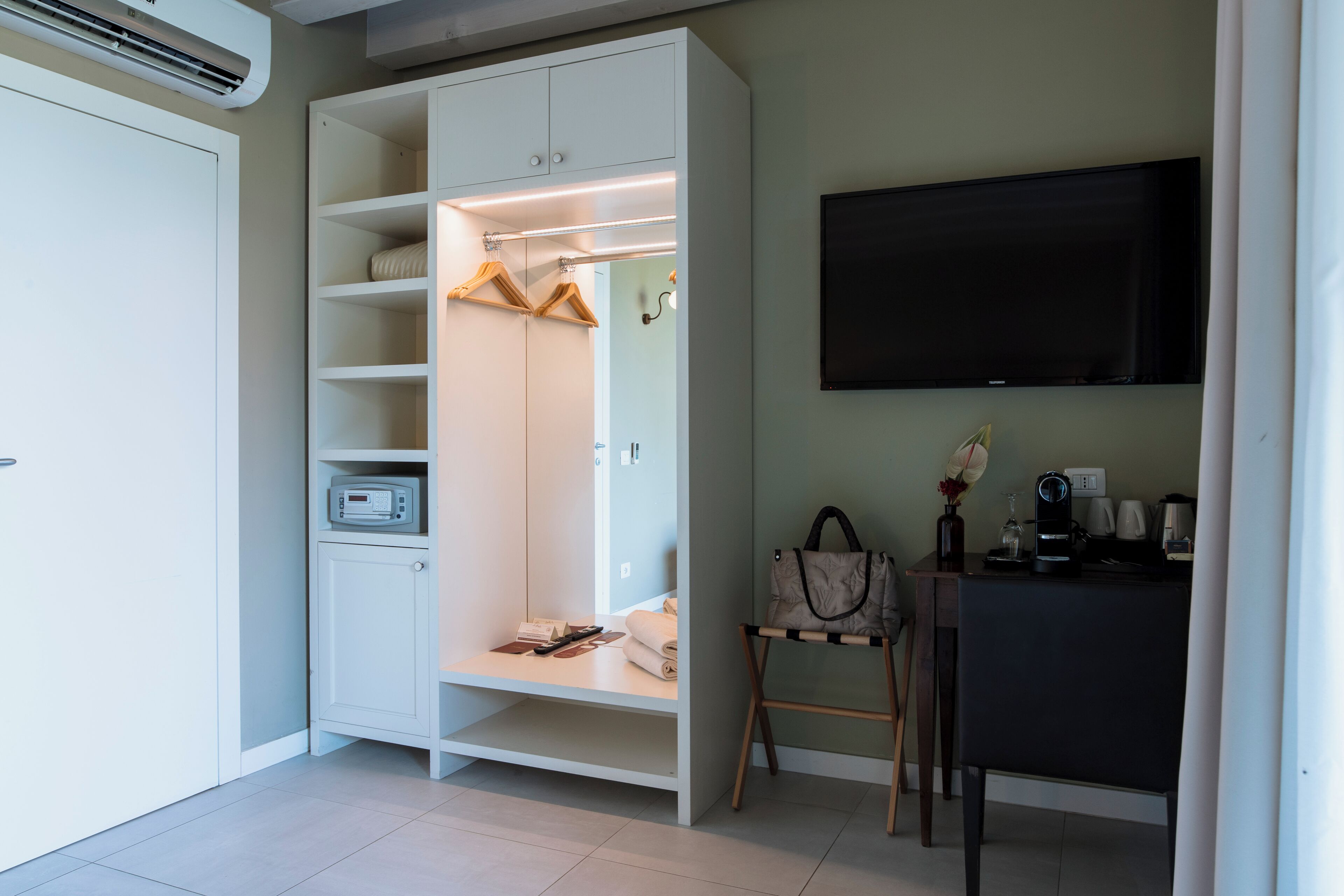 Habitación de hotel con vestidor, escritorio con silla, televisor de pantalla plana y cafetera.