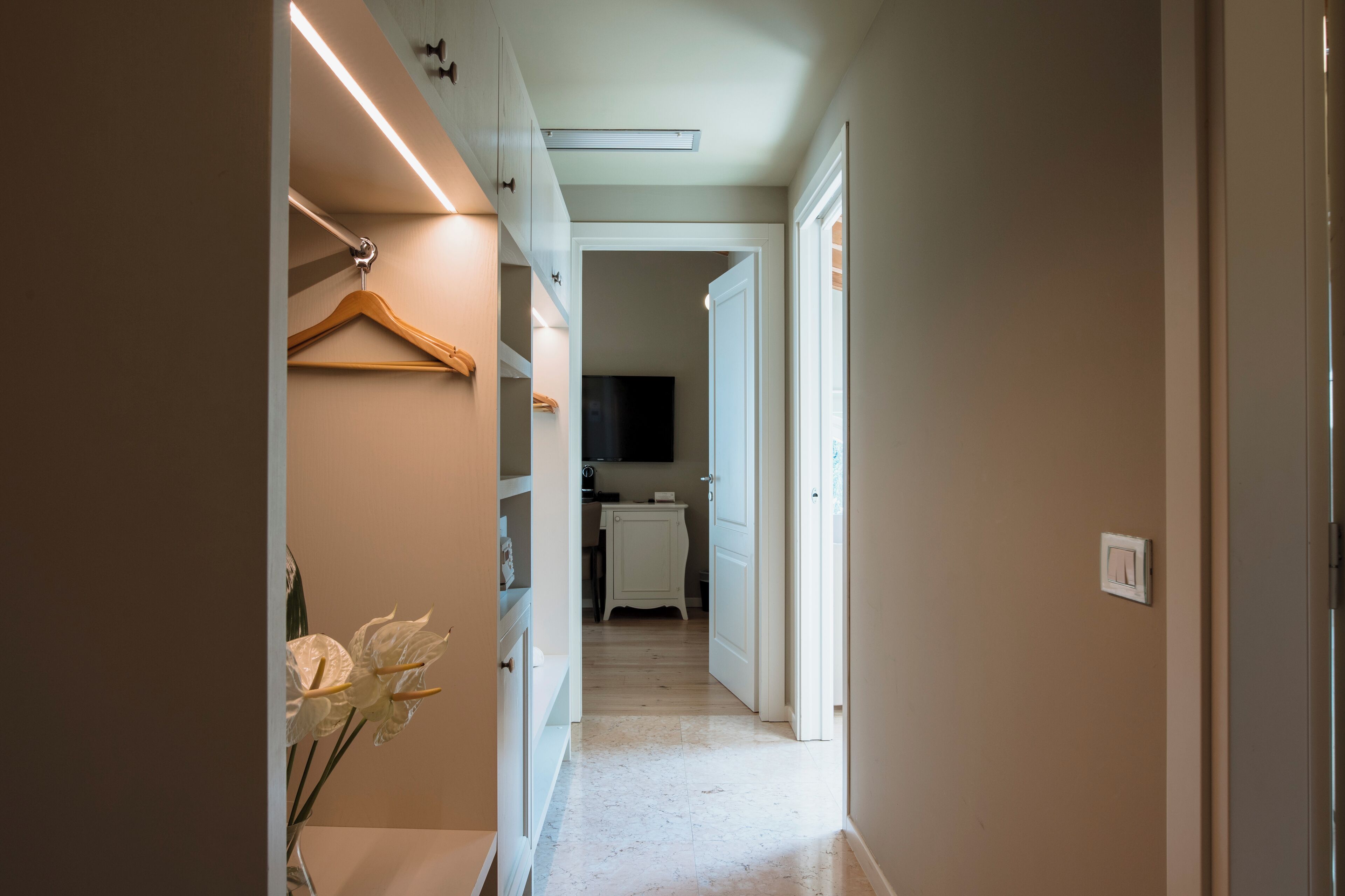 A narrow hallway with a wooden hanger and a vase of flowers on the left, leading to a kitchen area with a microwave and cabinets.