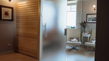 Una habitación con una puerta corredera, una silla blanca, una mesita con un florero y un cuadro en la pared.