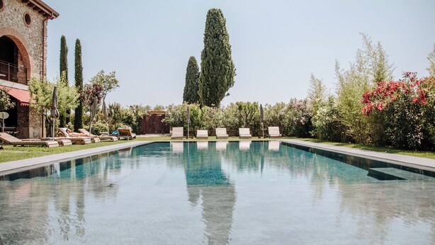 Une piscine avec des chaises longues et, en arrière-plan, un bâtiment en pierre.
