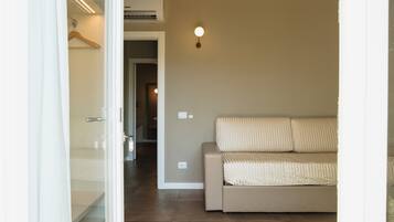 Une pièce avec un canapé beige, une porte en verre donnant sur un couloir et un luminaire fixé au mur.