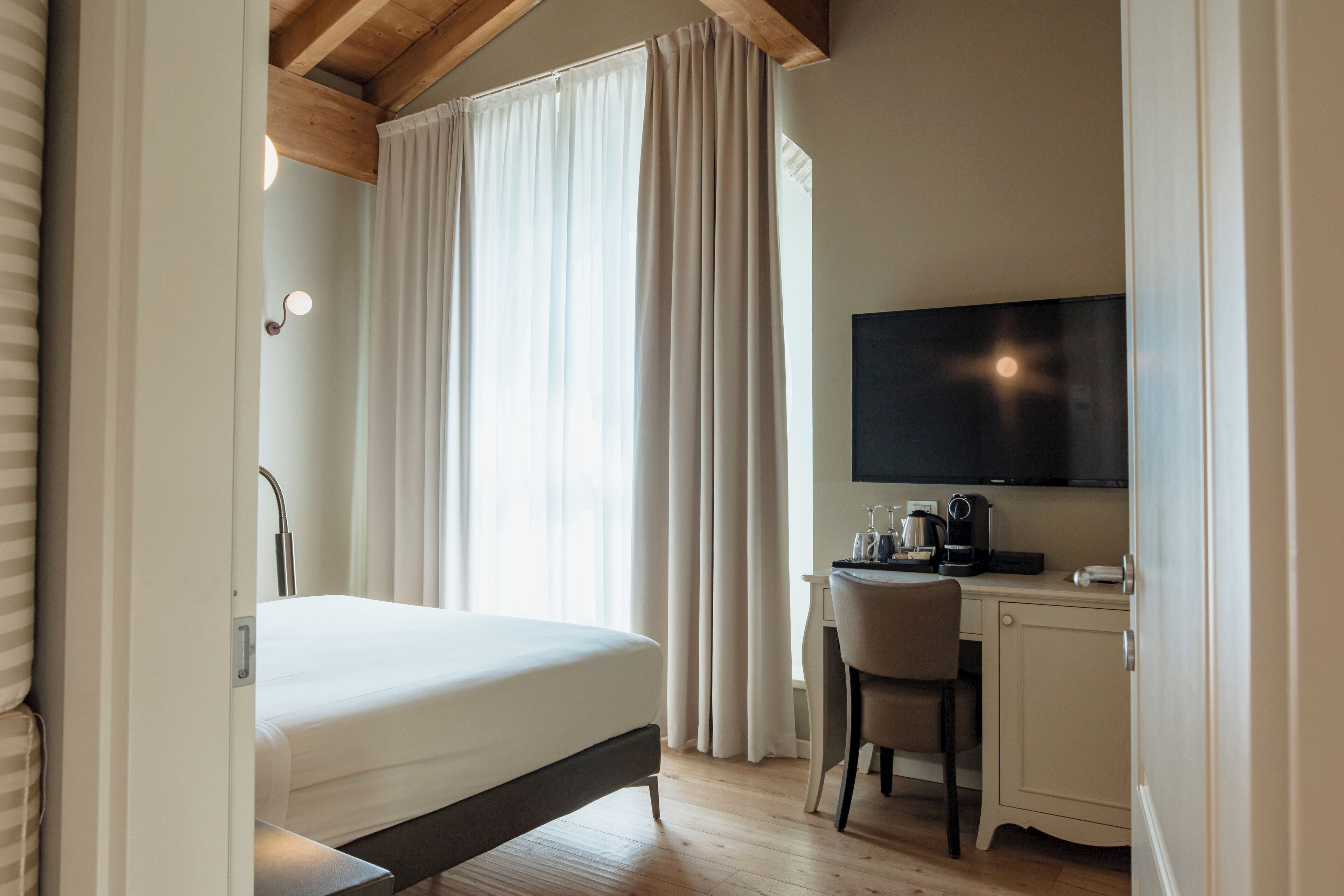 Una habitación de hotel con cama, escritorio con silla, televisor y ventana con cortinas.