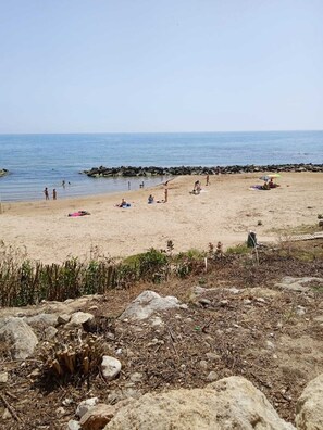Una playa con gente tomando el sol y nadando, una costa rocosa y un cielo despejado.