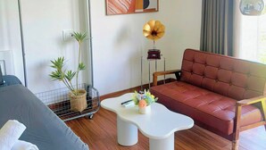 A modern hotel room with a bed, a sofa, a small coffee table, a potted plant, and a wall-mounted artwork. - Corgi House - Steps from Dragon Bridge (Da Nang)