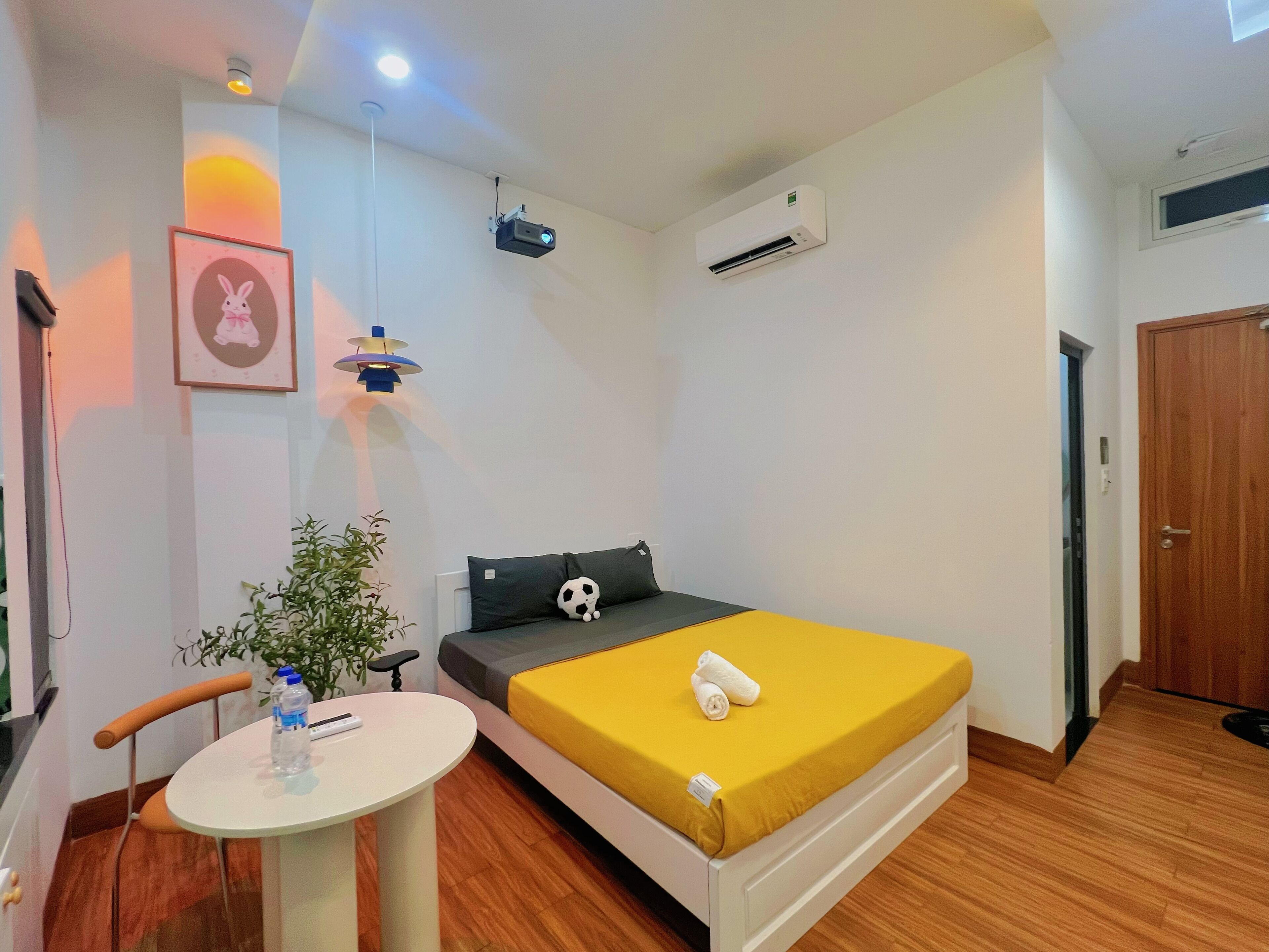 A bedroom with a bed, a desk, a chair, a potted plant, and a door.