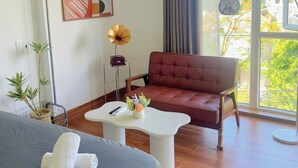 A modern room with a bed, a red leather sofa, a white coffee table, and a large window with a view of greenery. - Corgi House - Steps from Dragon Bridge (Da Nang)