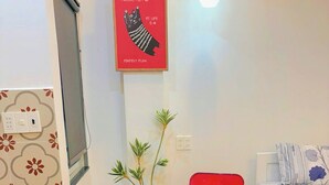 A compact room with a bed, a small table, a green chair, a red chair, a hanging light, and a poster on the wall. - Corgi House - Steps from Dragon Bridge (Da Nang)