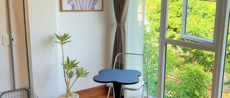 A room with a large window, a potted plant, a green chair, a small table, and a metal chair.
