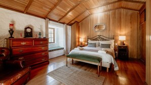 A cozy bedroom with a wooden ceiling, a bed with white linens, a wooden dresser, and a window with curtains. - Alojamento T1 Gerês-Junto ao Rio (São Miguel)