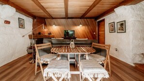 A cozy attic room with a wooden ceiling, a round wooden table, and cushioned seating. - Alojamento T1 Gerês-Junto ao Rio (São Miguel)