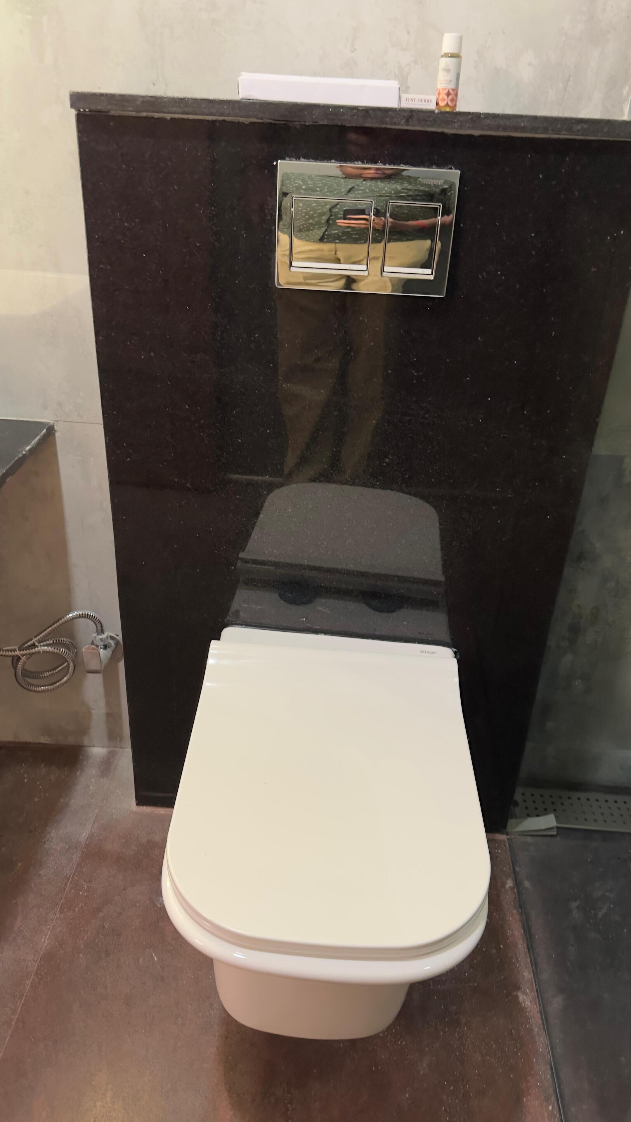 A toilet with a white seat and lid, a black vanity with a mirror, and a small bottle on top.