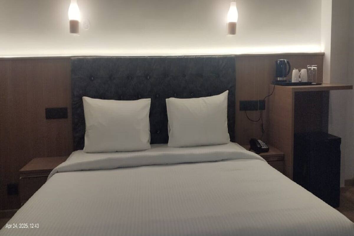A hotel room with a large bed, two bedside tables, a nightstand, a lamp, and a shelf with a coffee maker and glasses.