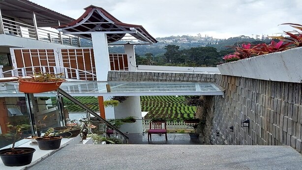 A modern building with a covered entrance, potted plants, and a view of a green landscape. - Calla Lily By The Brook (Kodaikanal)