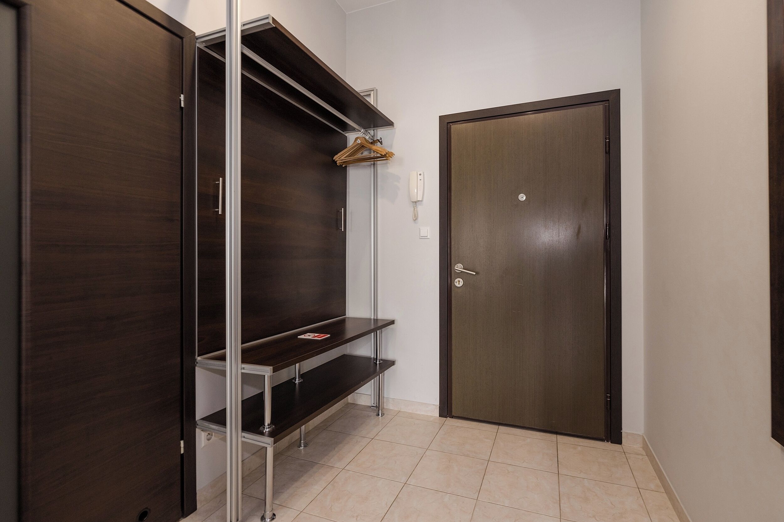 A room with a dark wooden wardrobe, a metal shelf unit, and a closed door.