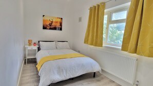 A bedroom with a bed, a nightstand, a window with curtains, and a wall-mounted picture.