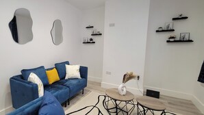 A modern living room with a blue sofa, decorative mirrors, and black shelves with framed pictures and plants.