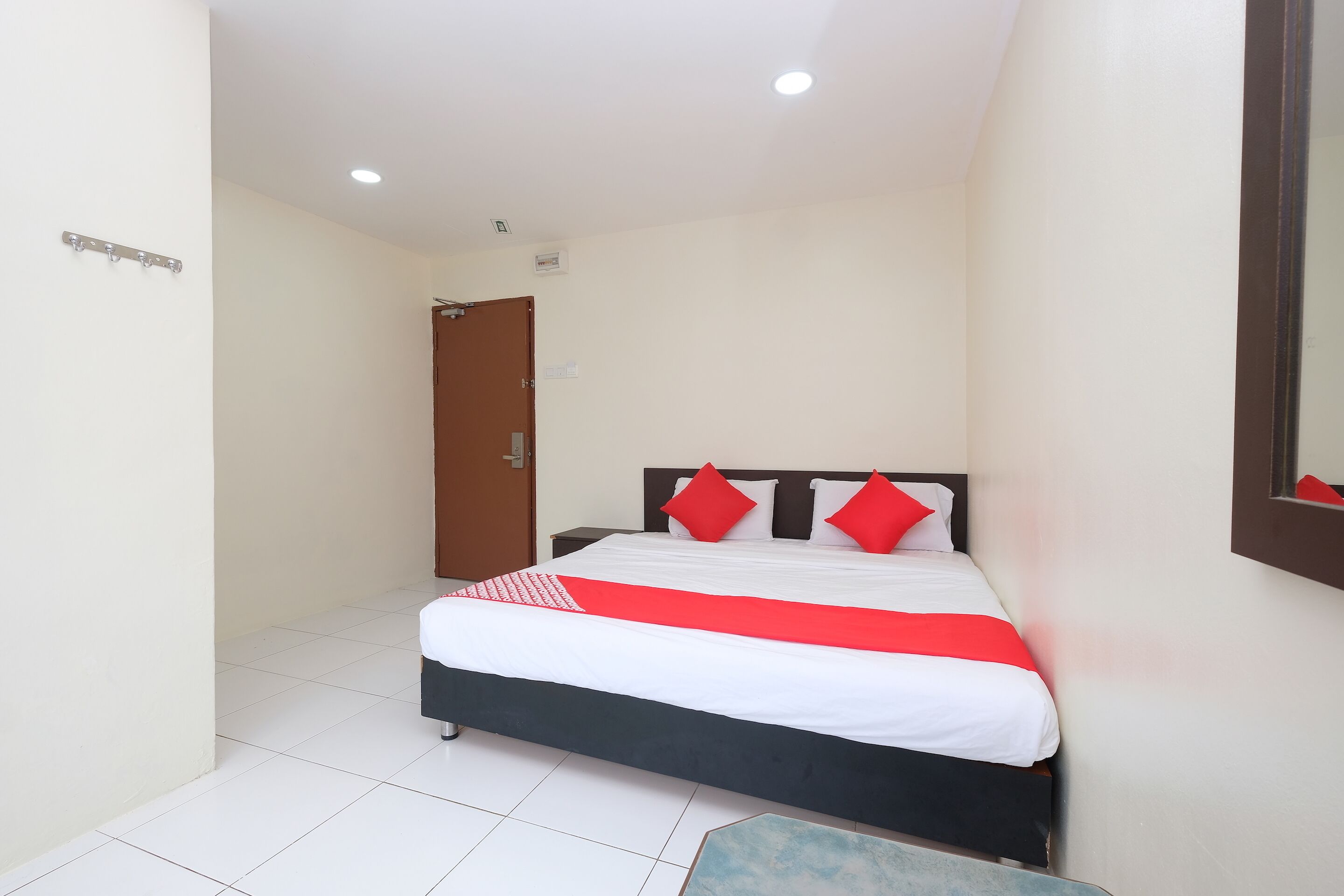A bedroom with a bed, a nightstand, a door, and a mirror on the wall.