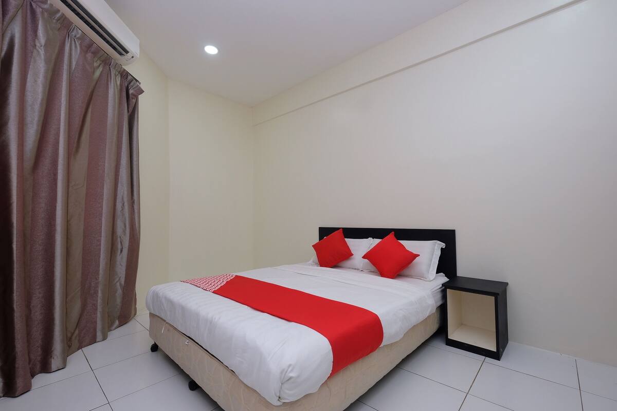 A neatly made bed with white and red bedding, a black nightstand, and a curtain on the left.