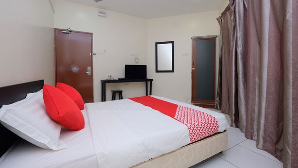 A neatly made bed with red and white bedding, a small desk with a chair, a mirror on the wall, and a door with curtains. - OYO 1104 Q Hotel (Temerloh)