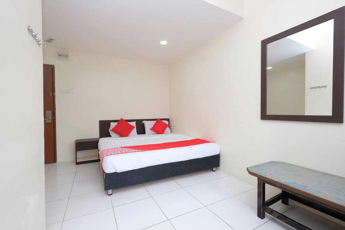 A hotel room with a bed, a bench, a mirror, and a door.