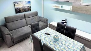 A modern living room with a grey sofa, a dining table with chairs, and a cityscape painting on the wall.