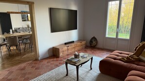 A living room with a TV, wooden cabinet, sofa, and dining area. - La Belle Fieffe - Garden, nature & peace (Vire Normandie)