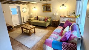 Un salon chaleureux avec des poutres apparentes, un canapé vert, une table basse en bois et un tapis à motifs.